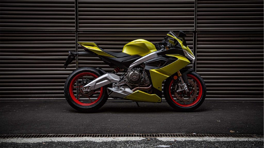 The side view of a bright-yellow 2021 Aprilia RS 660 in front of a garage door