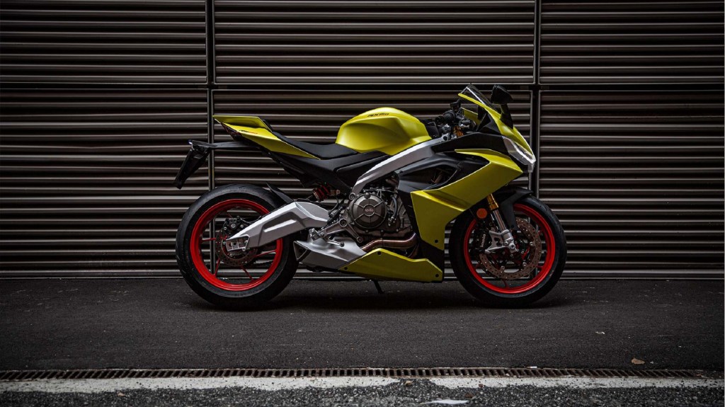 The side view of a bright-yellow 2021 Aprilia RS 660 in front of a garage door