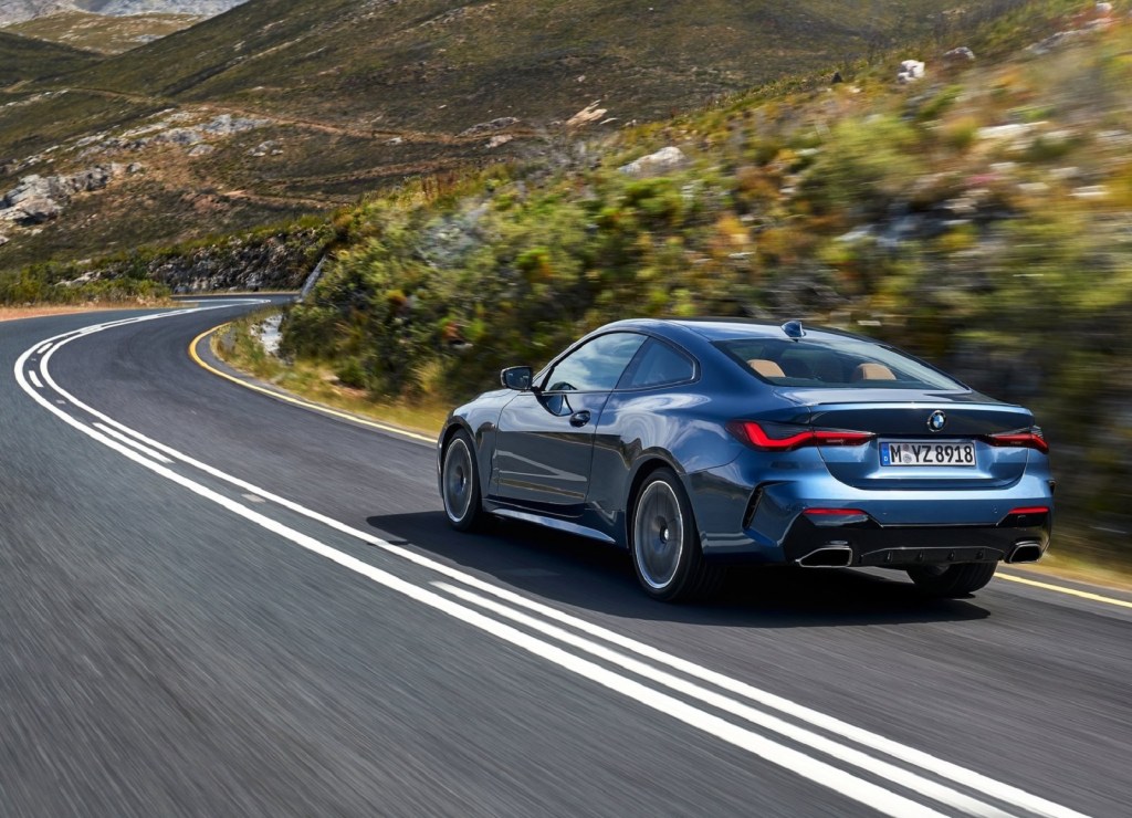 The rear view of a blue 2021 BMW M440i xDrive driving on a highland road