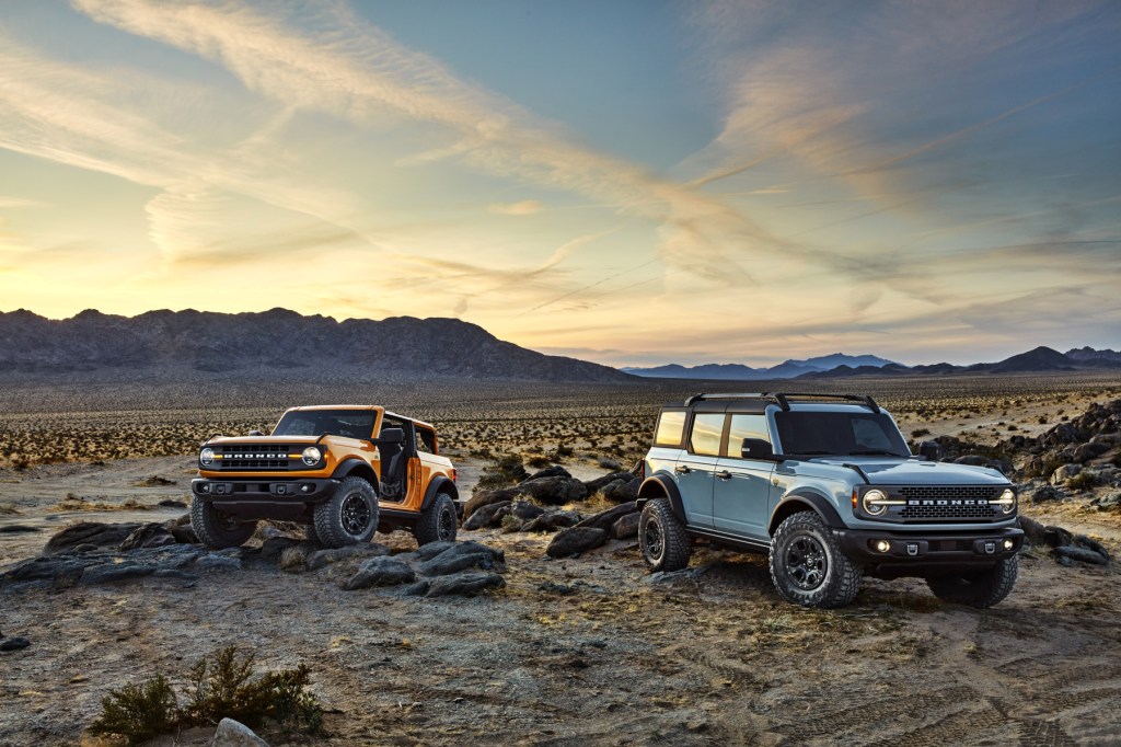 A pair of 2021 Ford Bronco SUVs parked on display over rugged terrain. One is a two-door model, and the other is a four-door model.