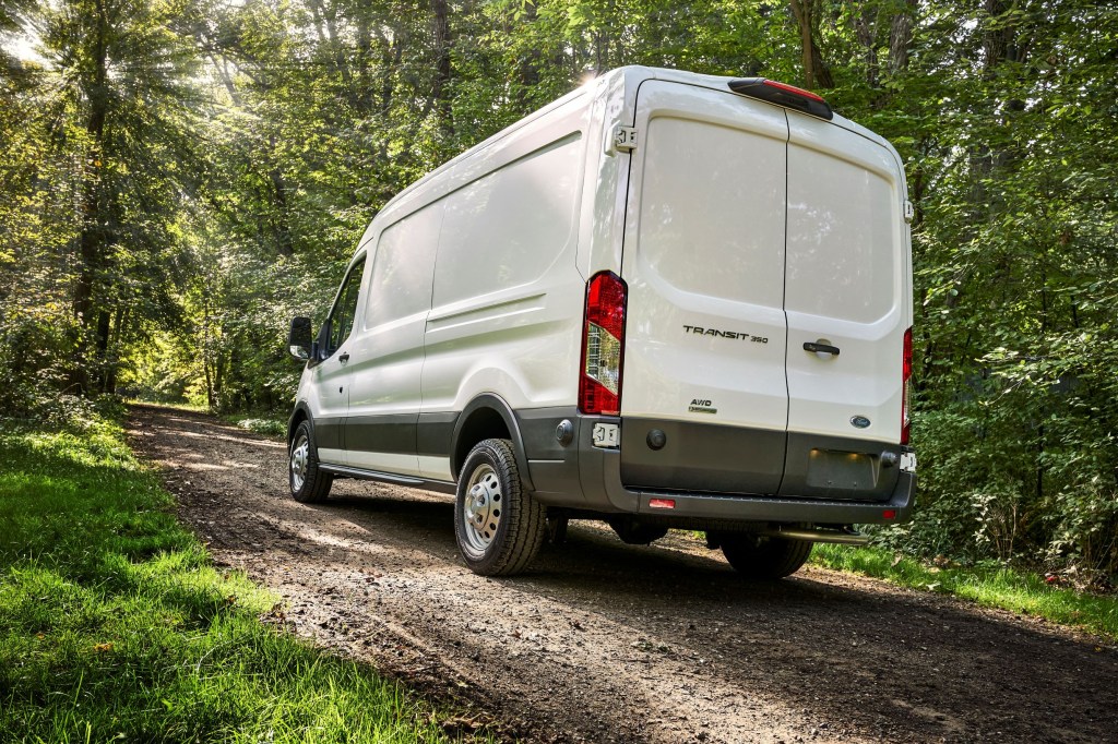 A white 2021 Ford Transit AWD with the Adventure Prep Package drives up a forest hill