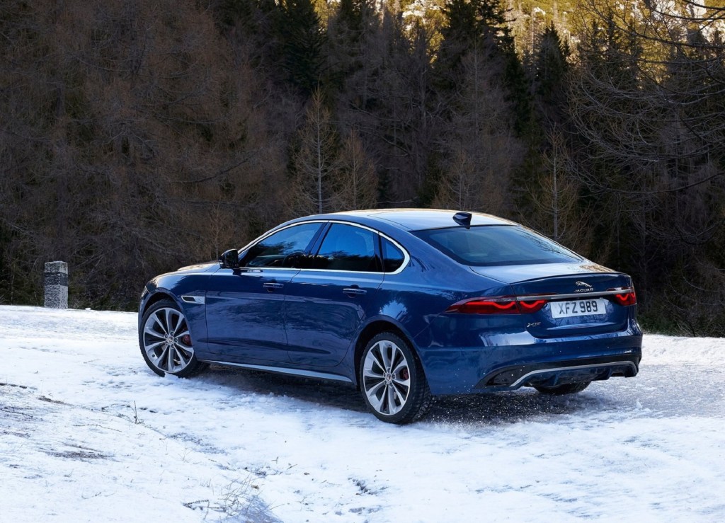 The rear 3/4 view of a blue 2021 Jaguar XF parked on a snowy forest hill