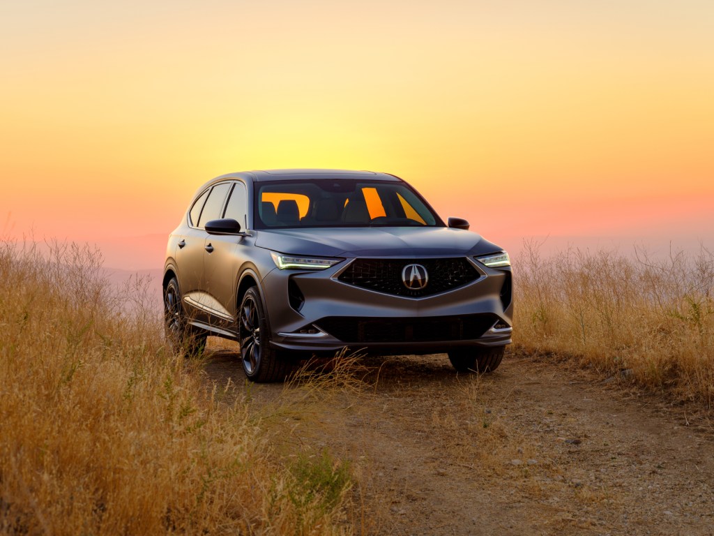 The 2022 Acura MDX prototype parked in a patch of grass with the setting sun in the background