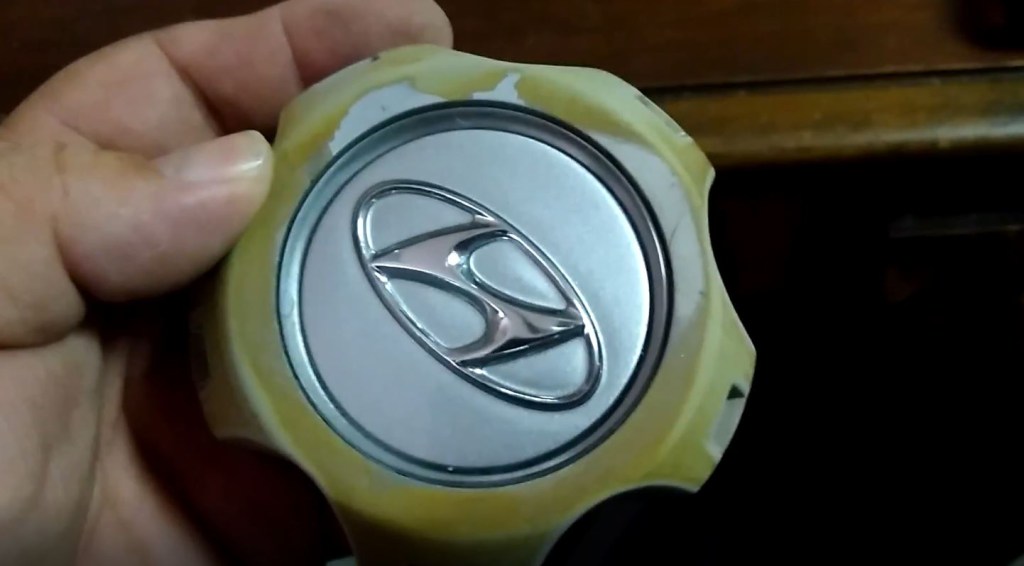 Wheel center cap froma 2005 Hyundai Tucson is missing paint and has yellowed with age