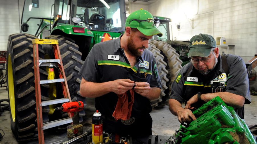 A master mechanic and service technician repair a John Deere tractor in a garage