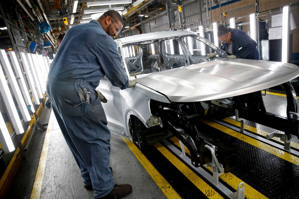 two people work in factory to assemble the hood of a Ford truck