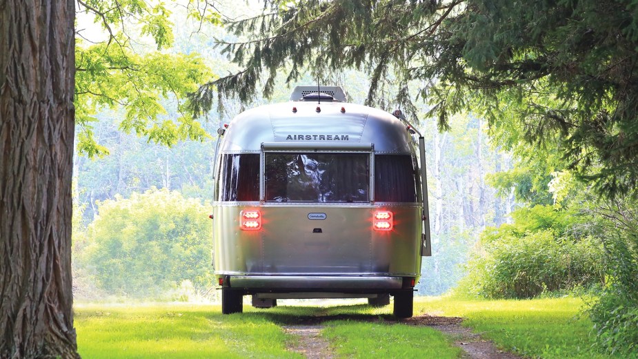 A gray Airstream Globetrotter camper off-road in the woods.