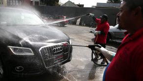 Two workers aim pressure washers at an Audi to clean off the paint finish