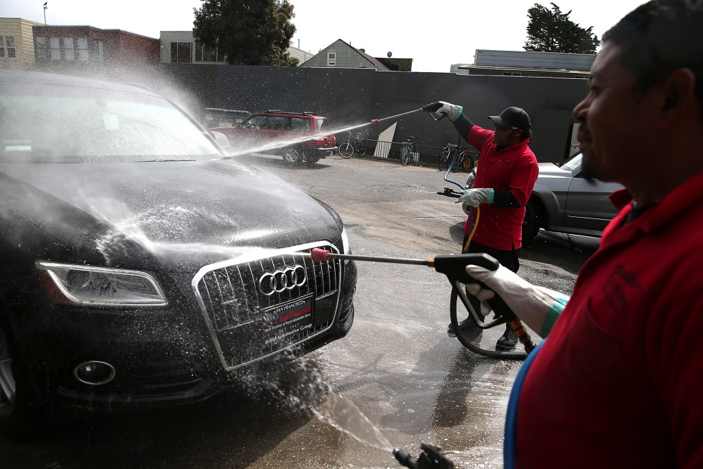 Two workers aim pressure washers at an Audi to clean off the paint finish