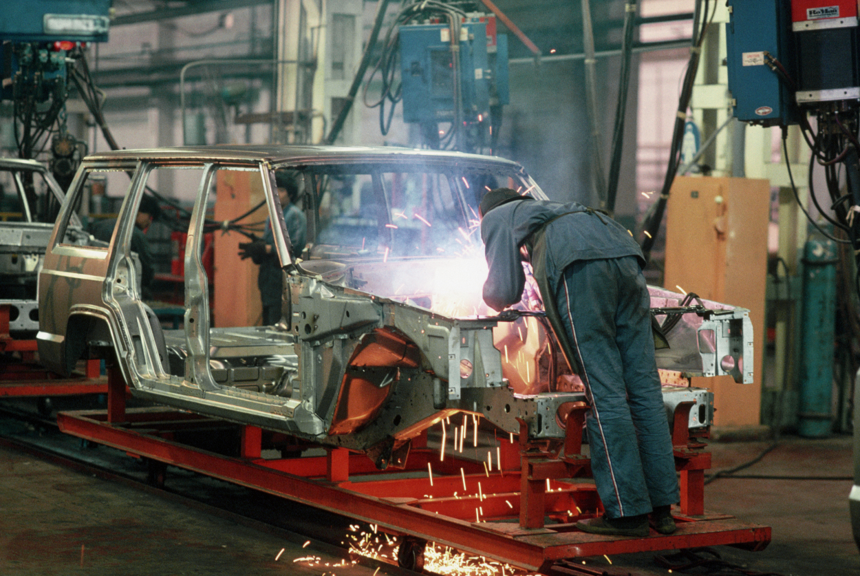 A welder in a Jeep factory goes to work on a frame