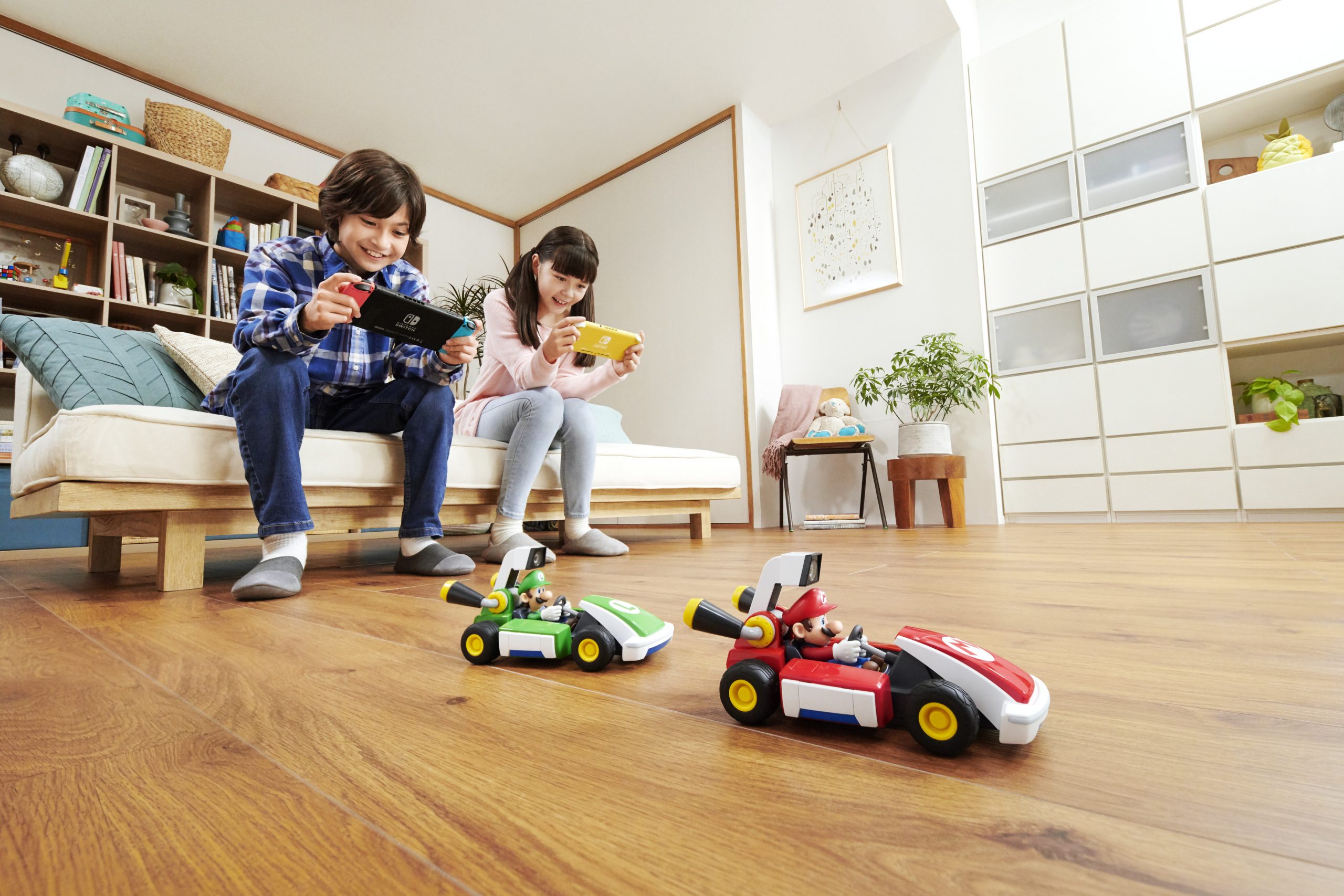 Two children holding Nintendo Switches as they control their vehicles for Mario Kart Live Home Circuit