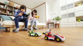 Two children holding Nintendo Switches as they control their vehicles for Mario Kart Live Home Circuit