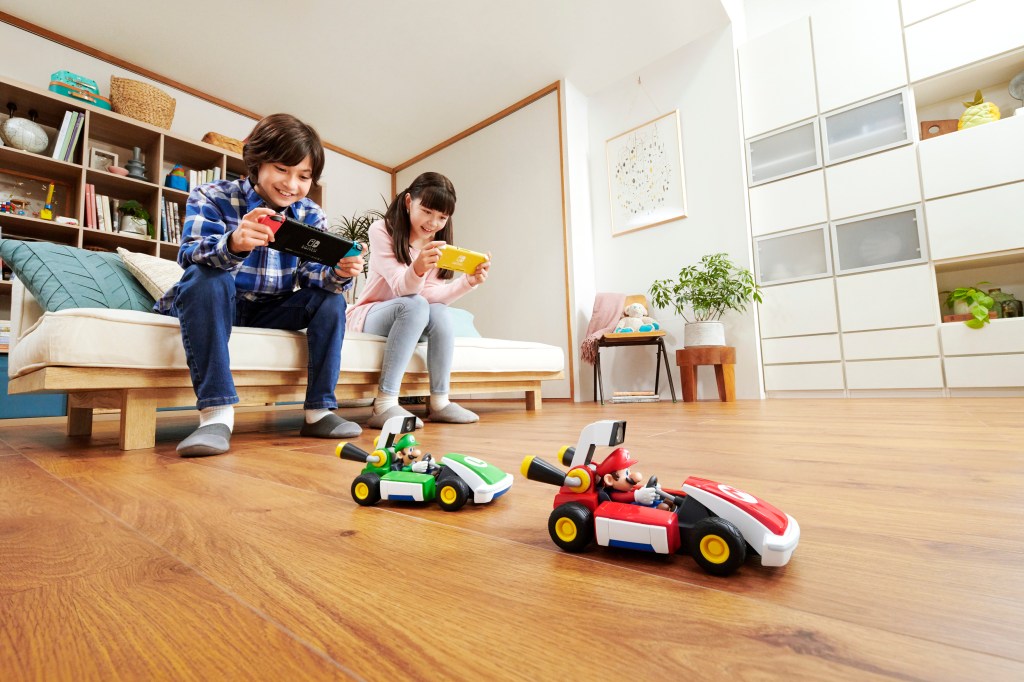 Two children holding Nintendo Switches as they control their vehicles for Mario Kart Live Home Circuit