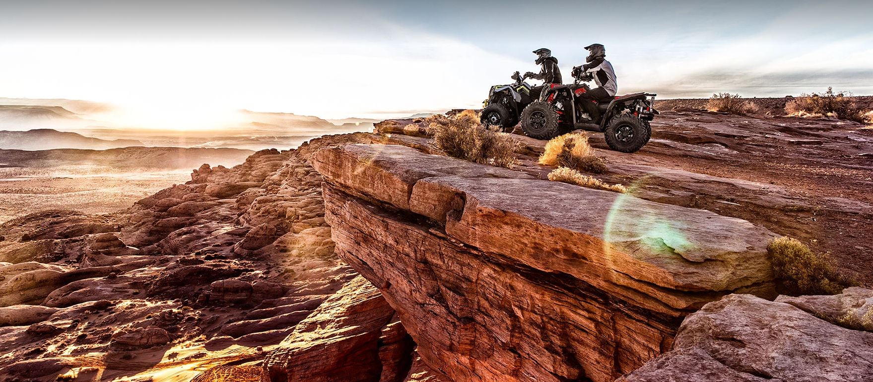 two Polaris Scrambler XP 10000 S ATV riders parked at the edge of a cliff watching the sunrise