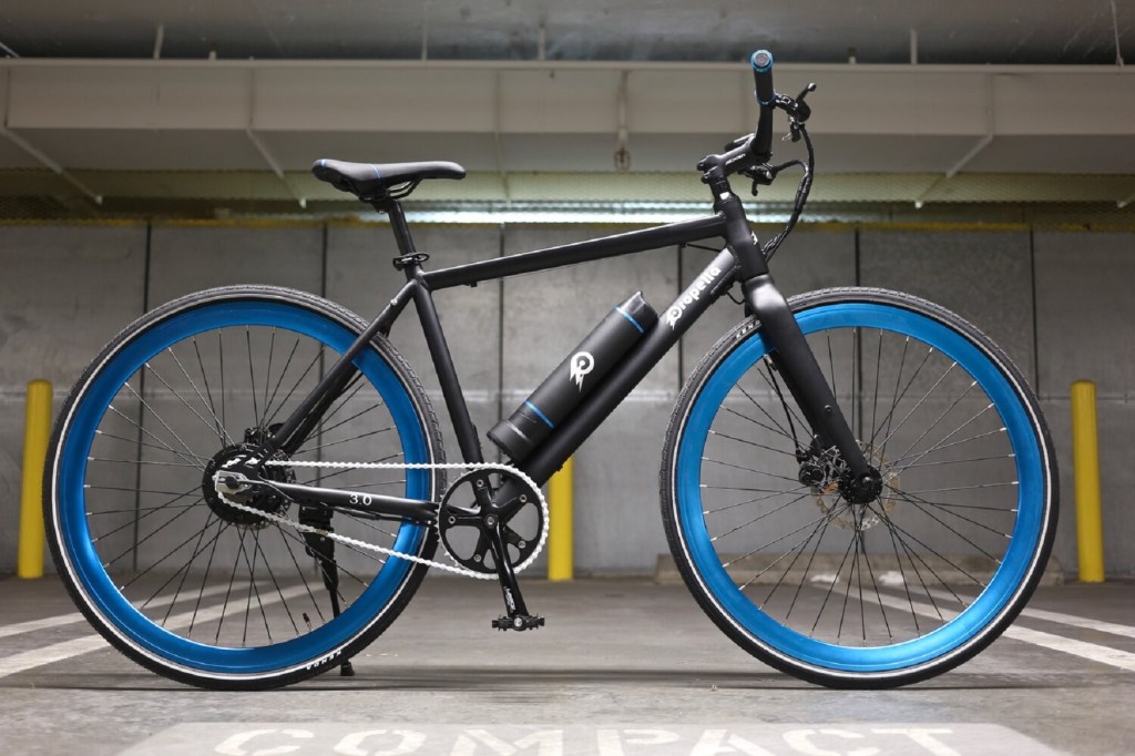 A black-framed blue-wheeled Propella 7-Speed Version 4.0 e-bike in a parking garage
