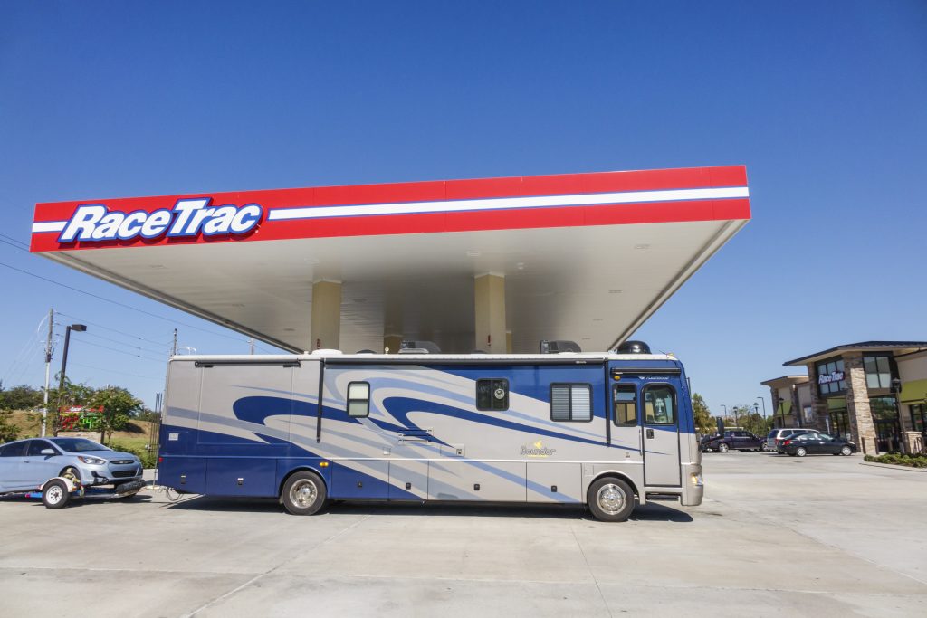 A full-size RV towing a car refuels under a gas station roof