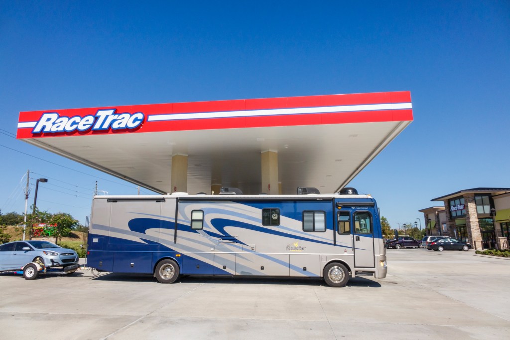 A full-size RV towing a car refuels under a gas station roof 
