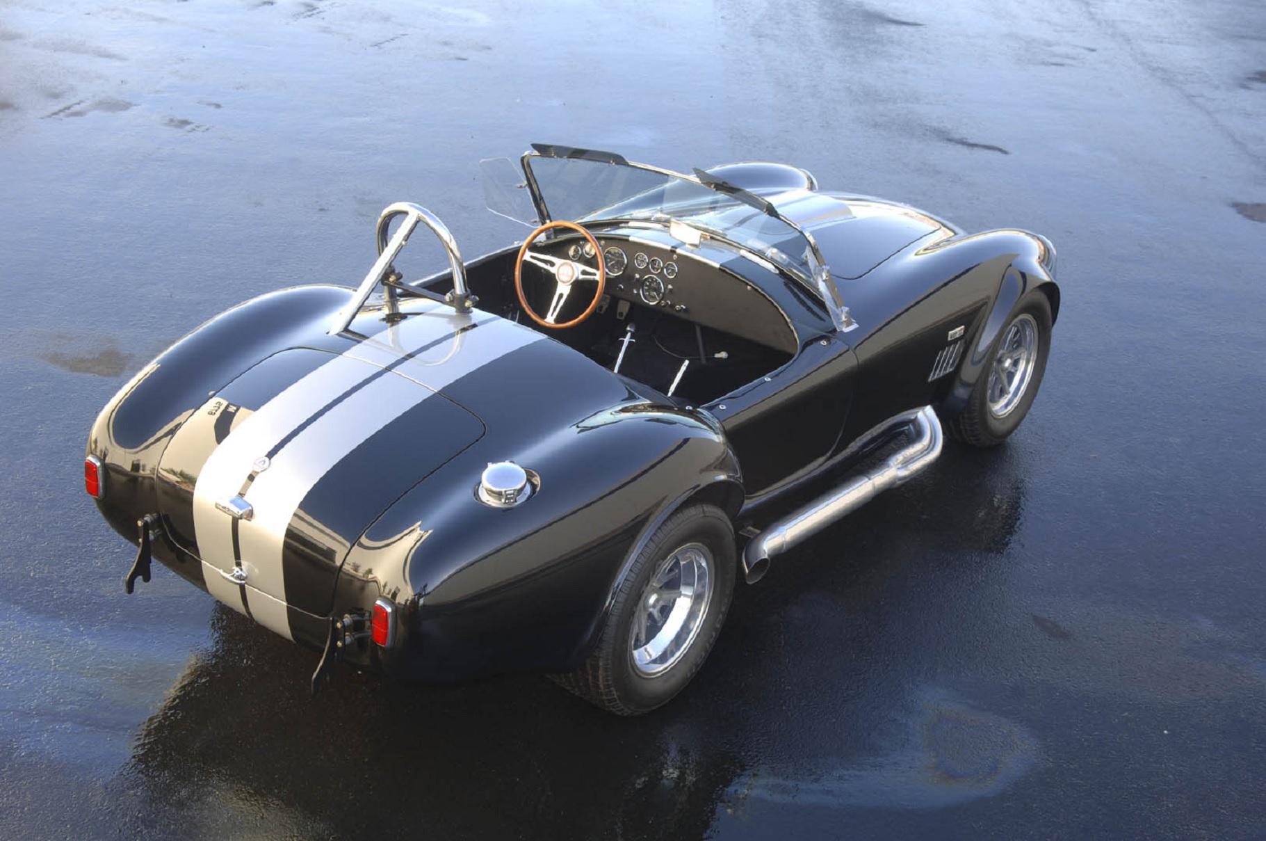The overhead rear 3/4 view of a gray-and-white Shelby Cobra 427 S/C CSX-Series 6000 continuation on a blacktop
