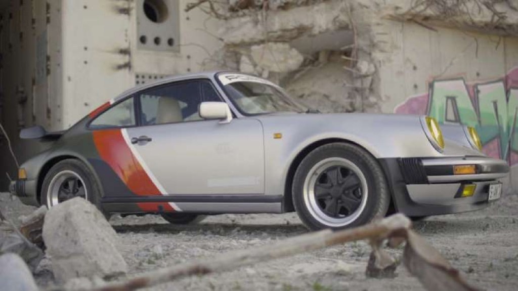 The silver-red-green Cyberpunk 2077-inspired 1977 Porsche 930 911 Turbo next to a graffitied concrete wall
