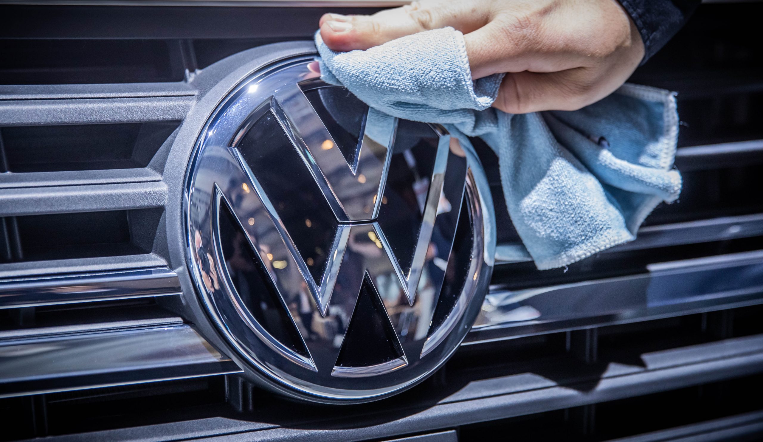 A person shines a Volkswagen logo on the grille of a car