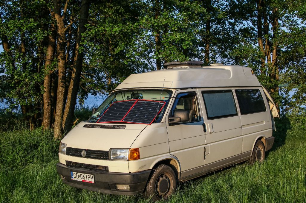 A beige Volkswagen T4 camper van with a flexible solar panel in the windshield