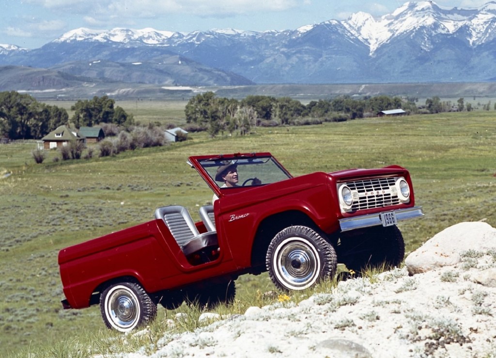 A red 1966 Ford Bronco Roadster climbs a rocky mountain hill