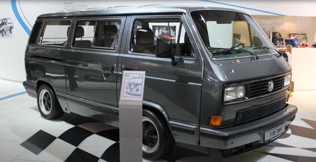 A charcoal colored 1985 Porsche B32 Minivan is on display in a museum.