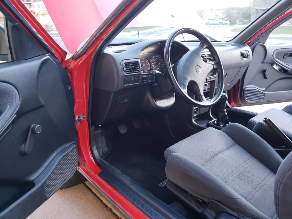 The black front seats and dashboard of a 1991 Nissan Sentra SE-R seen through the door