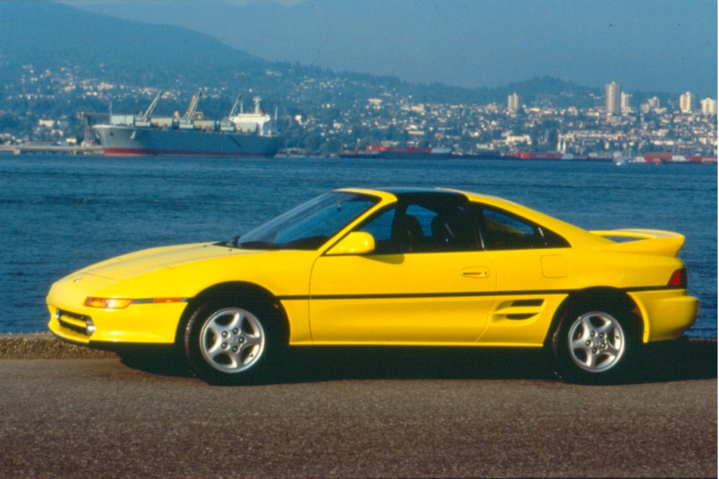 The side view of a yellow 1992 Toyota MR2 by a harbor