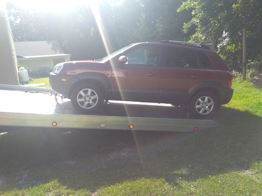 A burgundy 2005 Hyundai Tucson is loaded on a flat-bed tow truck