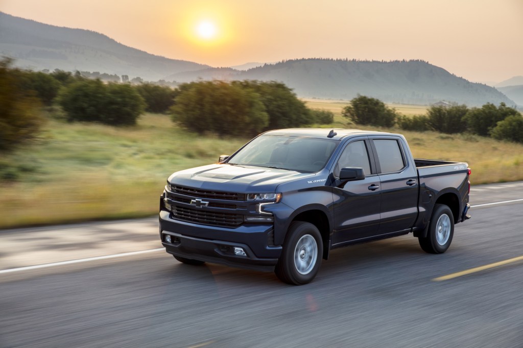 A blue 2020 Chevy Silverado 1500 driving on a road with a mountain range in the background