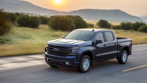 A blue 2020 Chevy Silverado 1500 driving on a road with a mountain range in the background