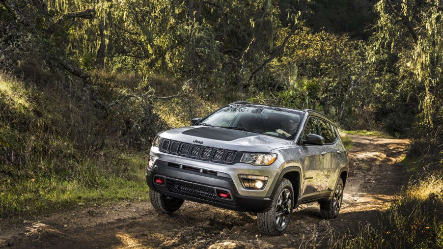 A silver 2020 Jeep Compass driving down a trail in the woods