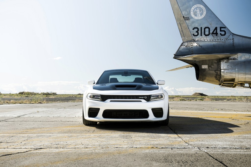 A white and black 2021 Dodge Charger Hellcat Redeye on display next to an airplane