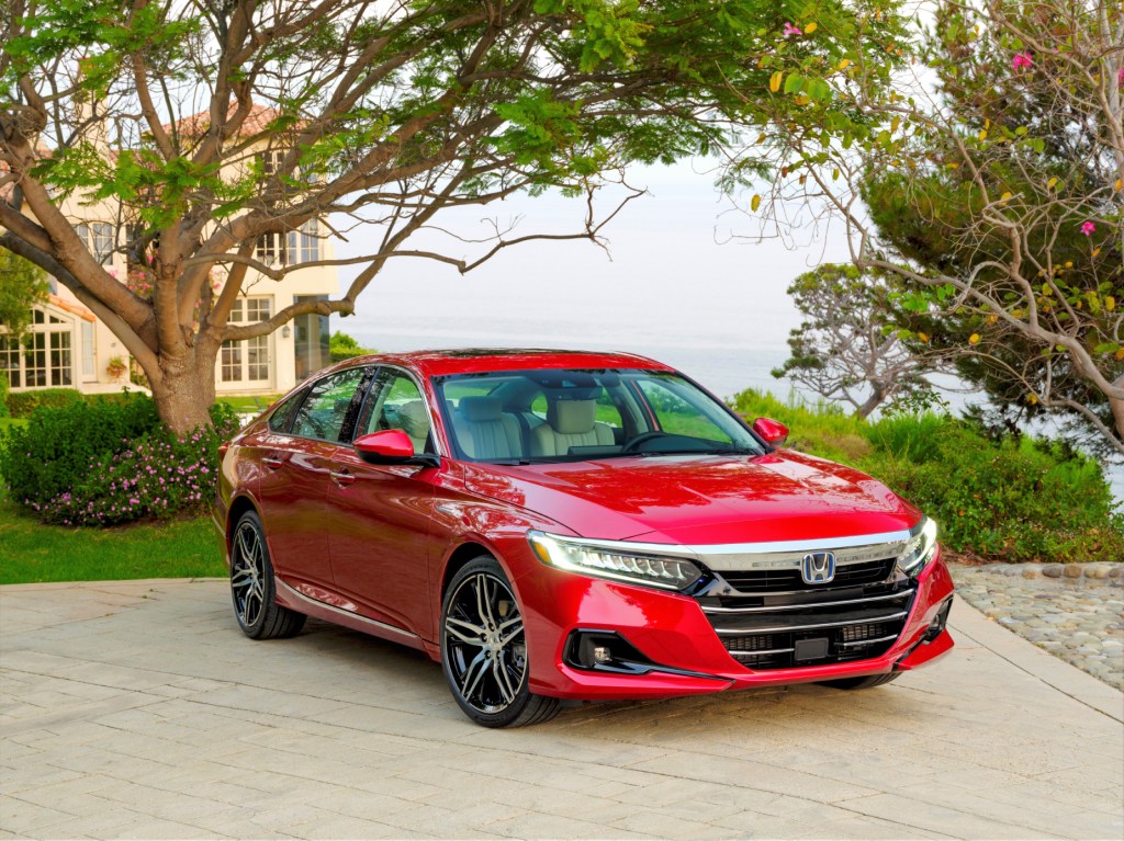A red 2021 Honda Accord Hybrid parked in front of a house with trees in the background