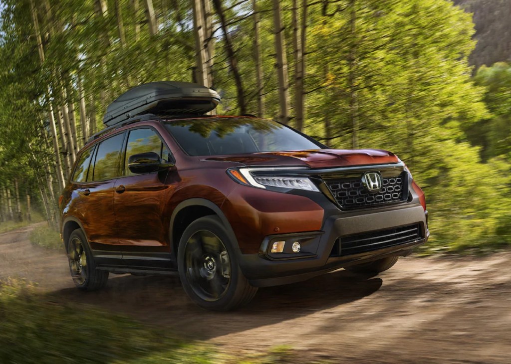 A red 2021 Honda Passport Elite AWD with a roof box drives through a forest