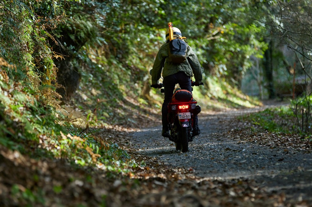 A rider takes a red 2021 Honda Trail 125 on a gravel forest trail