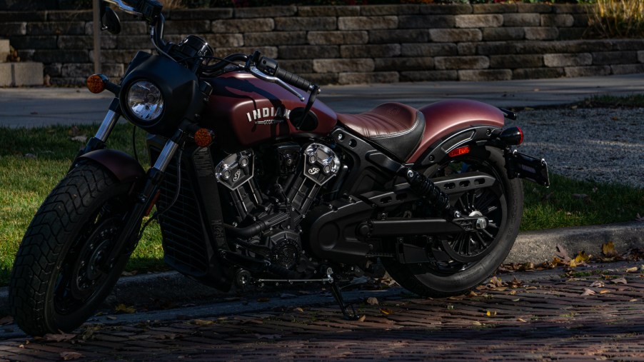 The front 3/4 view of a maroon 2021 Indian Scout Bobber on a shady street