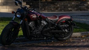 A maroon 2021 Indian Scout Bobber parked on a shady cobblestone road