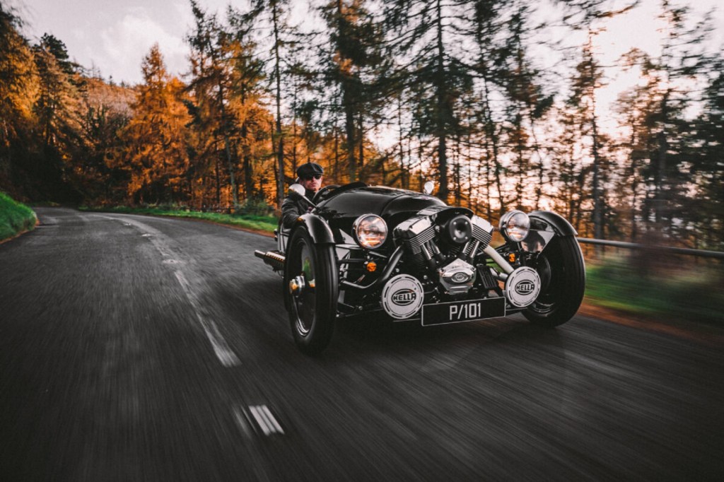 A black-and-white 2021 Morgan 3-Wheeler Belly Tank drives through a fall forest