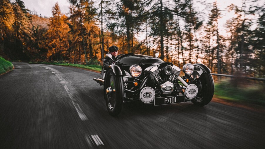 A black-and-white 2021 Morgan 3-Wheeler Belly Tank drives through a fall forest