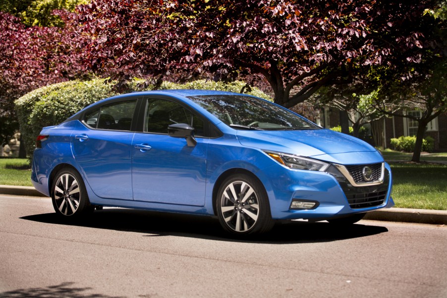 A blue 2021 Nissan Versa parked in front of some colorful trees