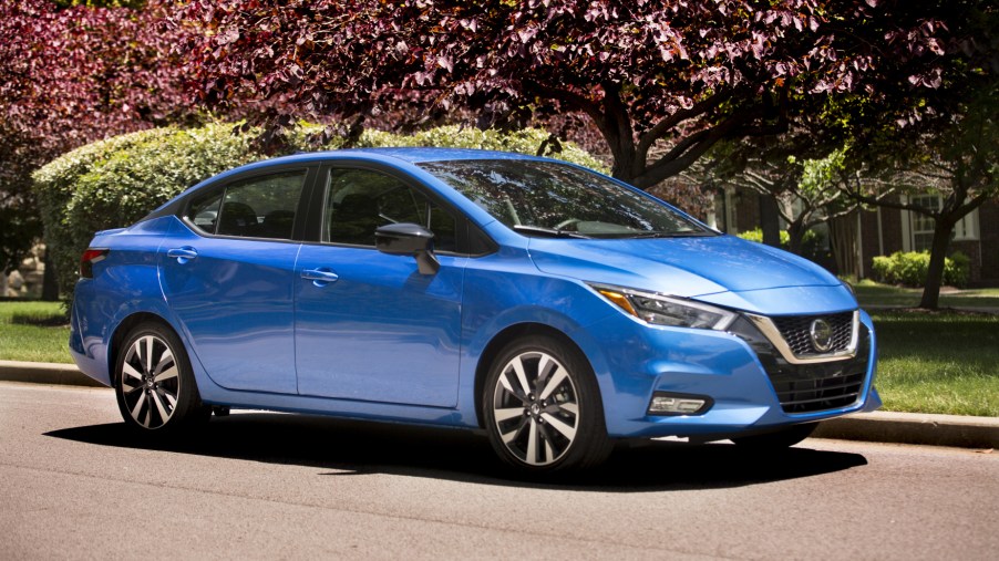 A blue 2021 Nissan Versa parked in front of some colorful trees