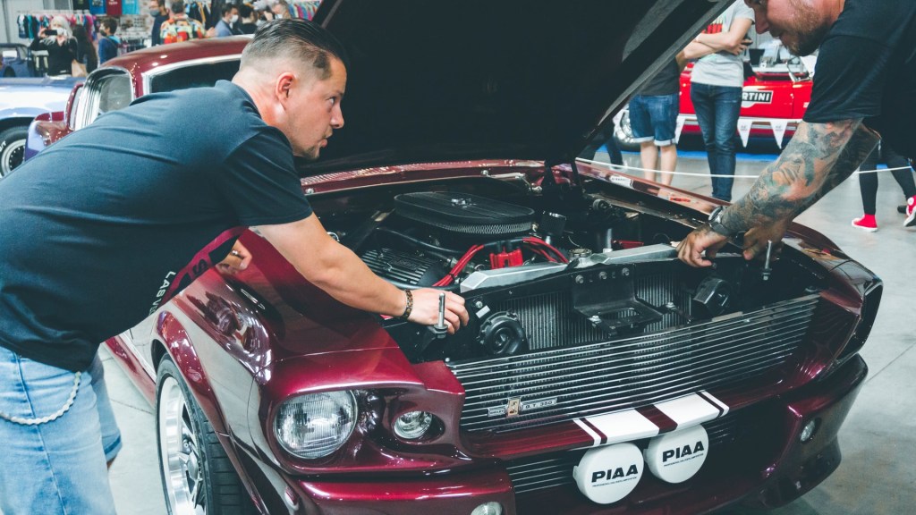 Two mechanic inspecting an engine of a red classic car.