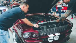 Two mechanic inspecting an engine of a red classic car.