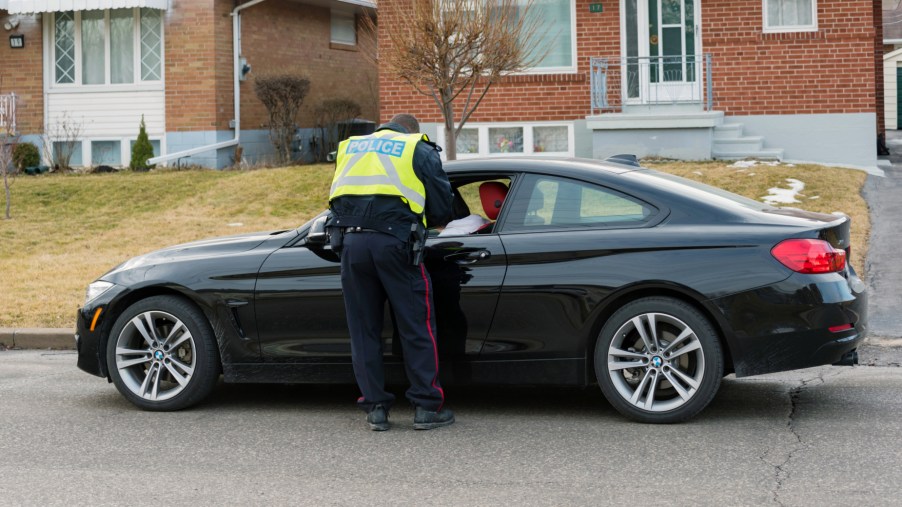 A cop giving a speeding ticket to a driver in a black sedan