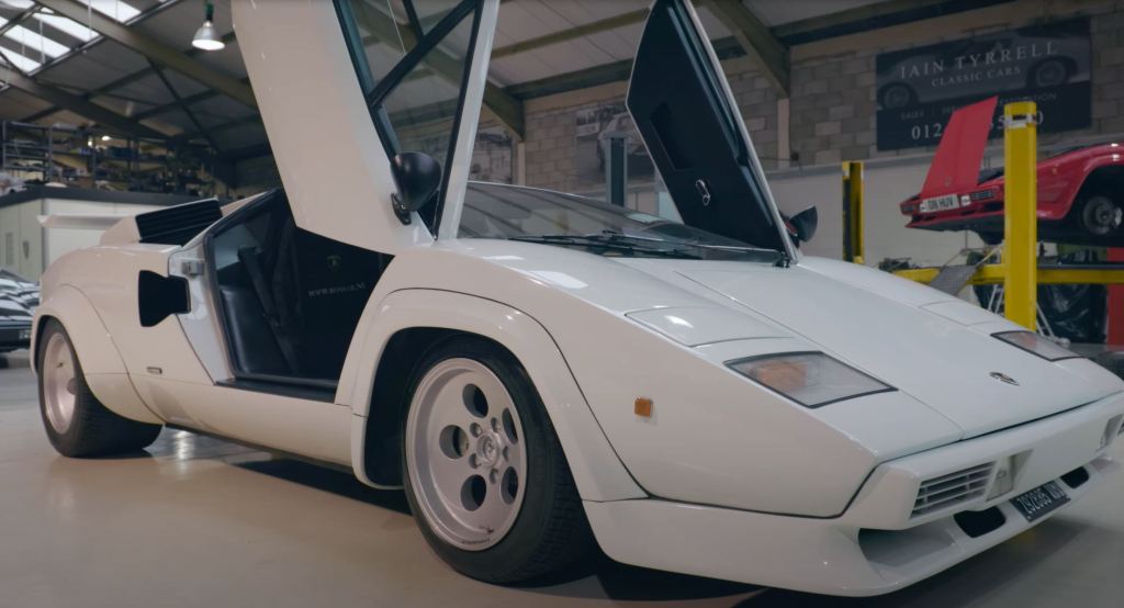 A white Lamborghini Countach sits in a shop with its doors swung up.