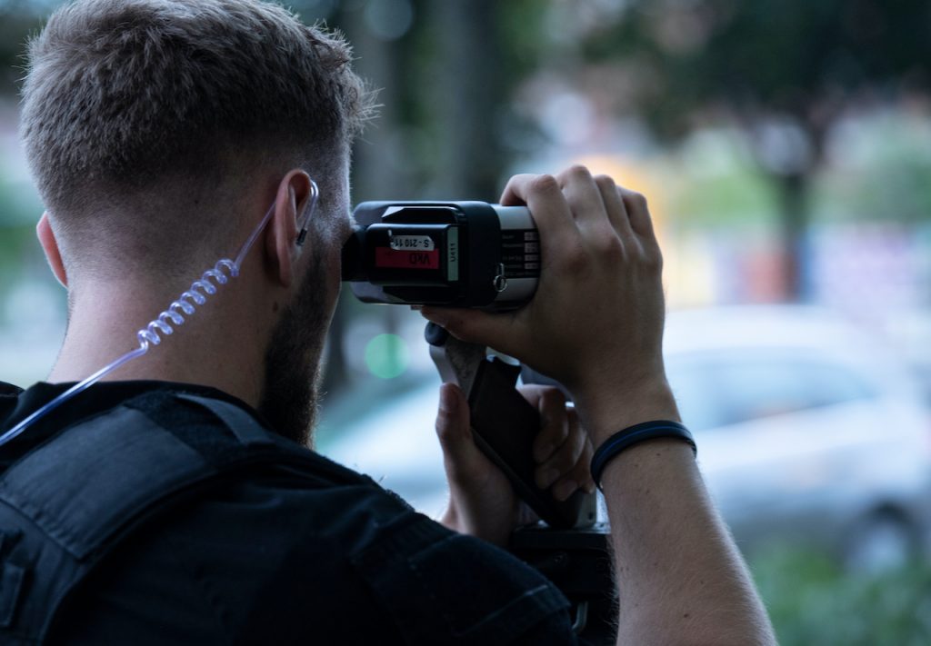 A photo of a police officer in a speed trap looking through a radar gun.