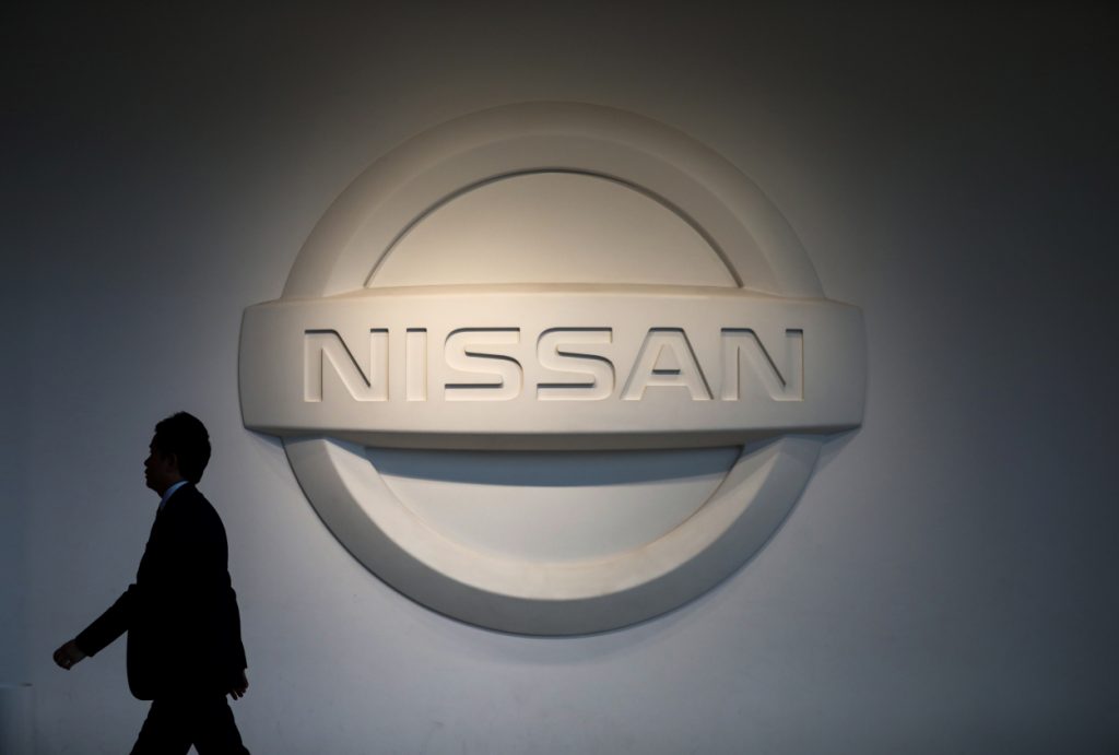 A man walking past the a big Nissan logo on a wall