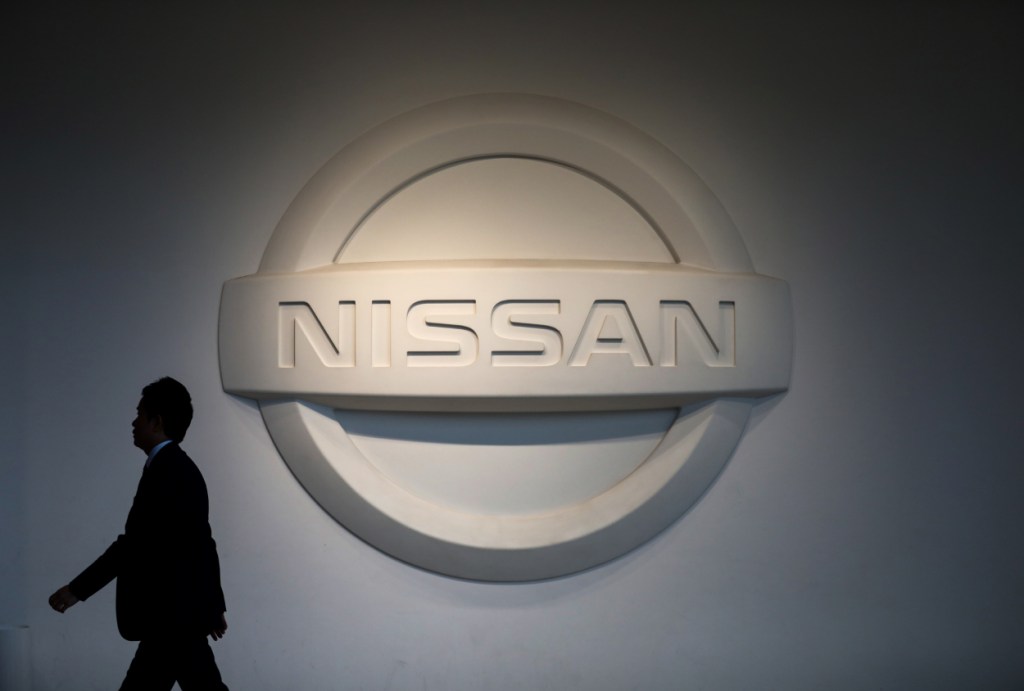 A man walking past the a big Nissan logo on a wall